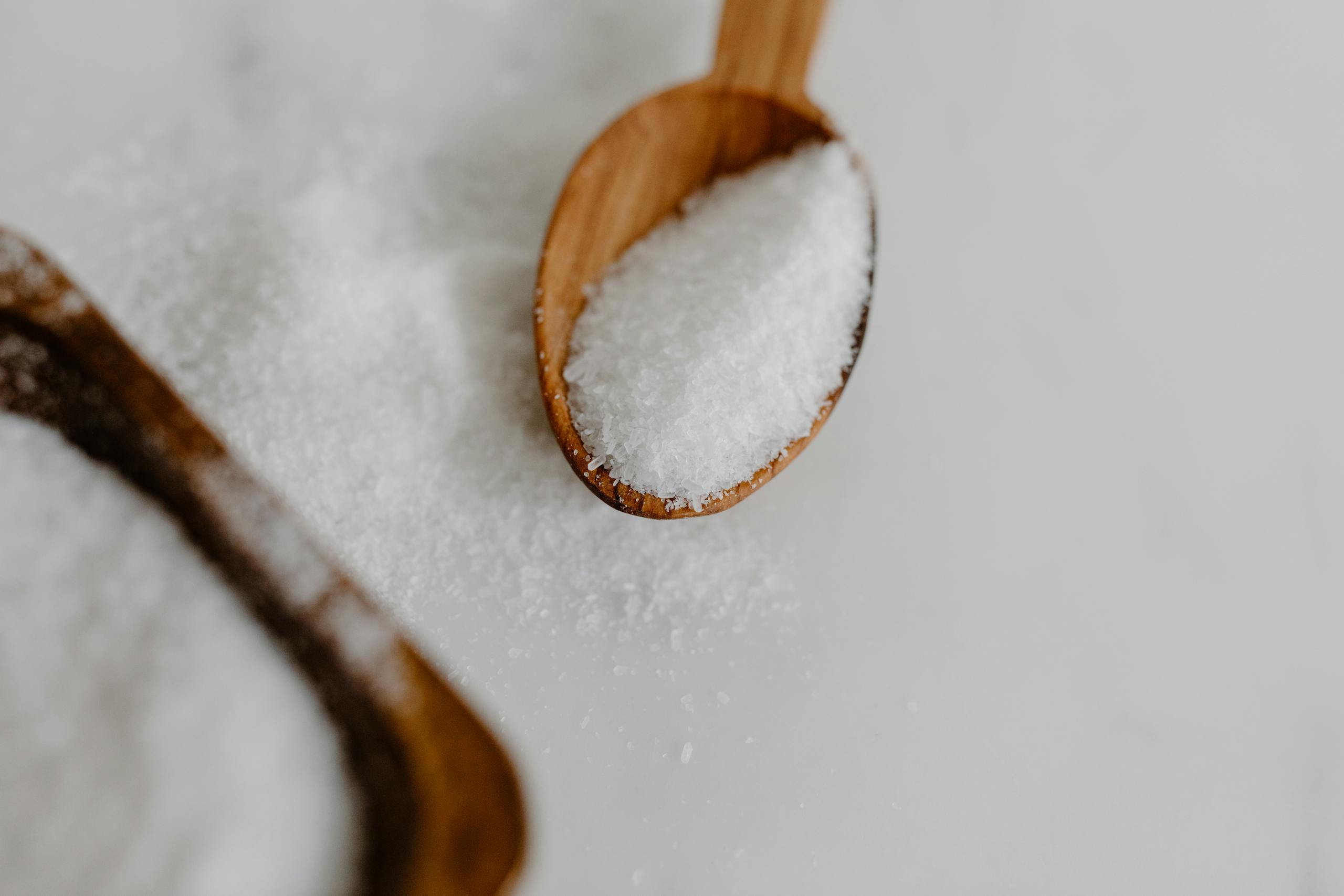 A close-up image of granular salt in a wooden spoon, perfect for culinary themes.