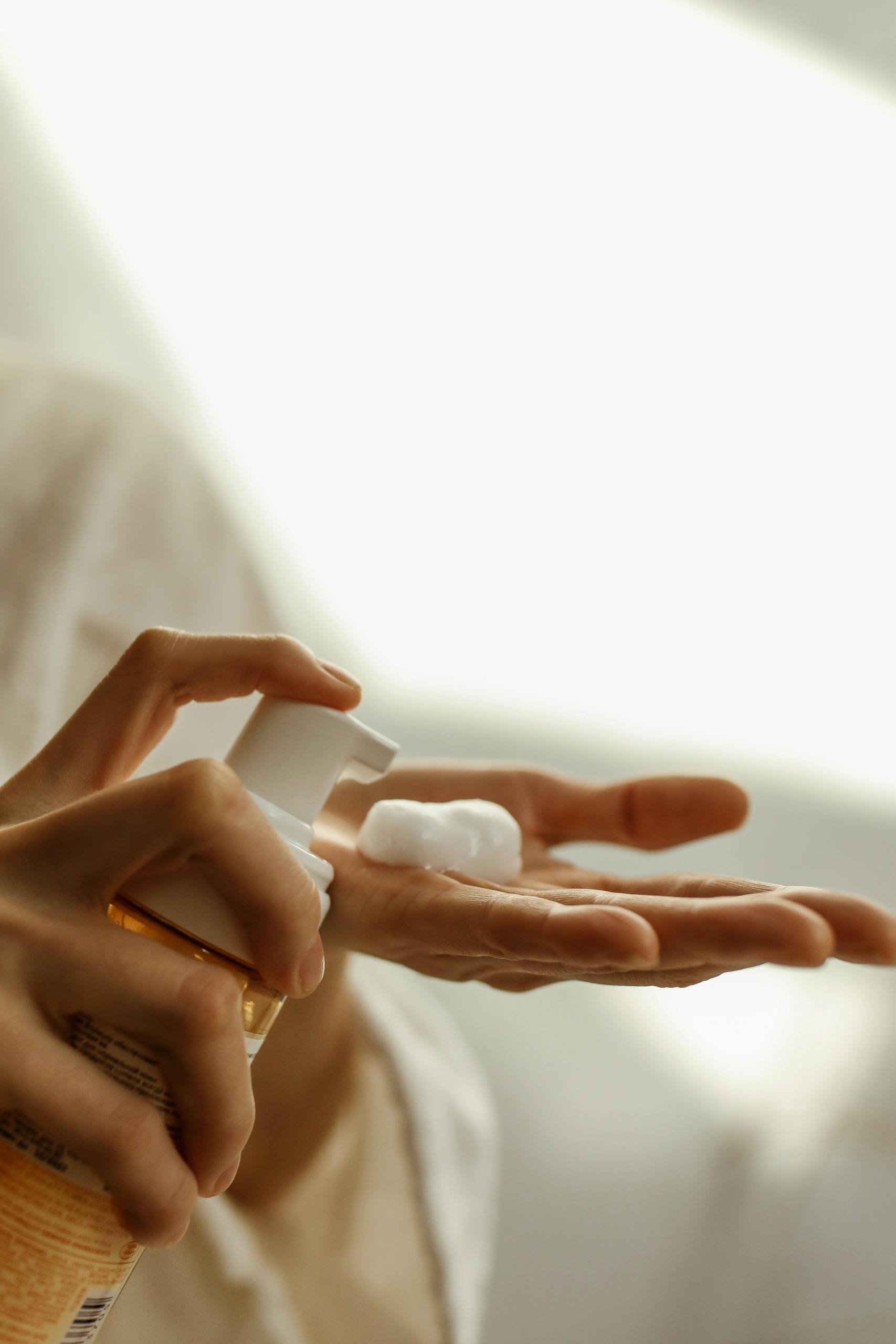 A detailed close-up of hands using a pump dispenser to apply skincare foam.