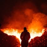 A person silhouetted against a fiery volcanic eruption, observing the intense lava flow.