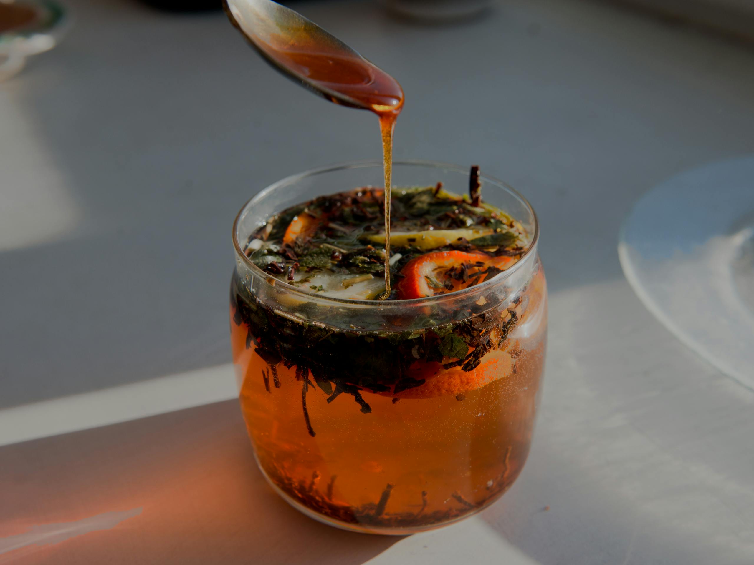 Close-up of a citrus herbal tea with honey being drizzled from a spoon, capturing warm sunlight.