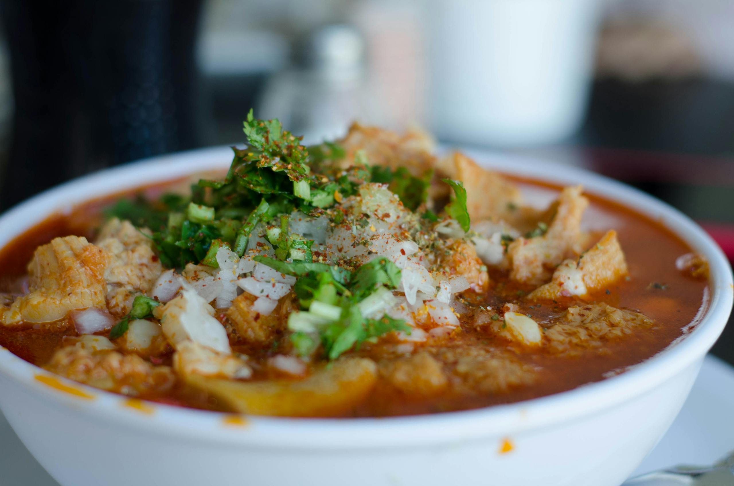 Close-up of a delicious Mexican menudo soup garnished with fresh herbs in a white bowl.