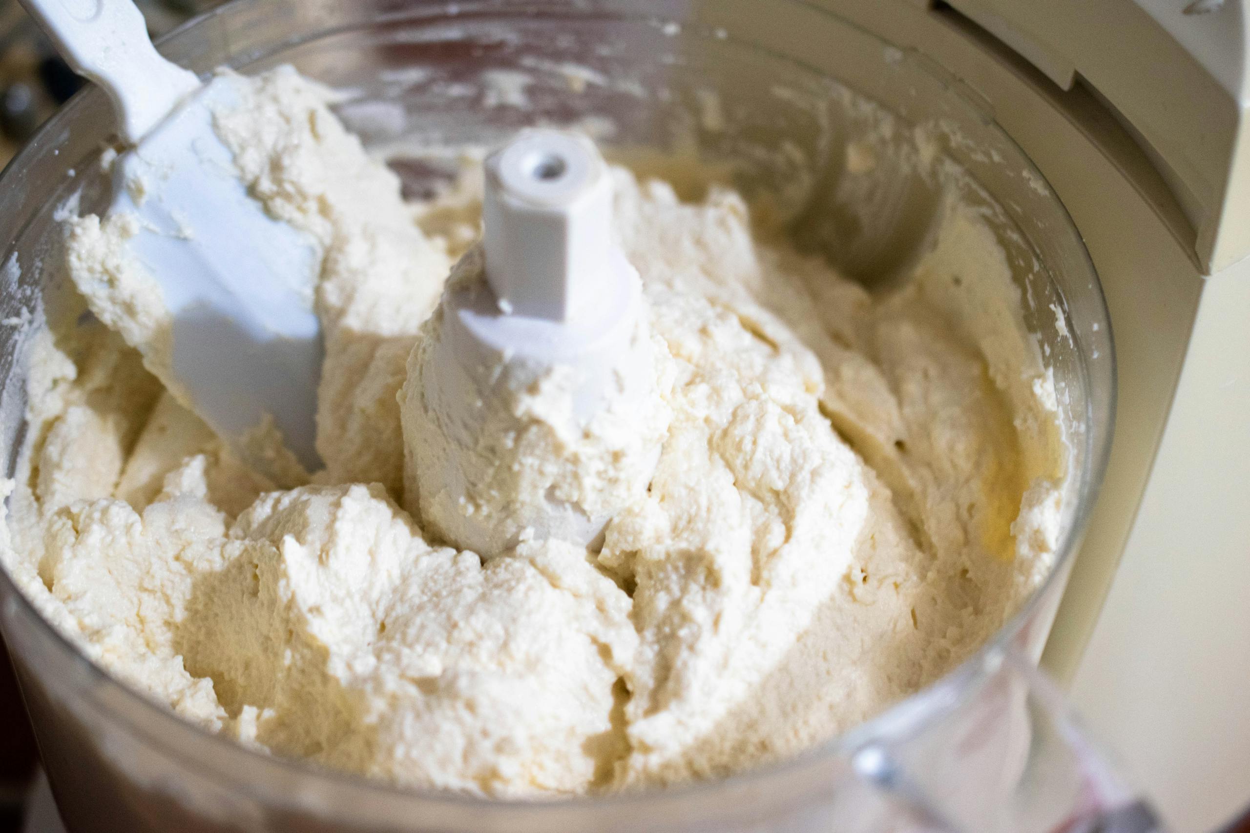 Close-up of creamy cheese batter being mixed in a food processor, perfect for baking needs.