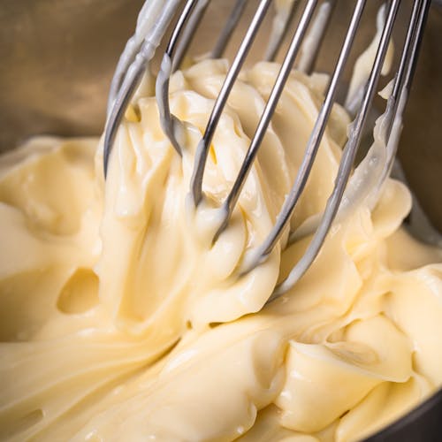 Close-up of homemade mayonnaise being whisked in a metal bowl.