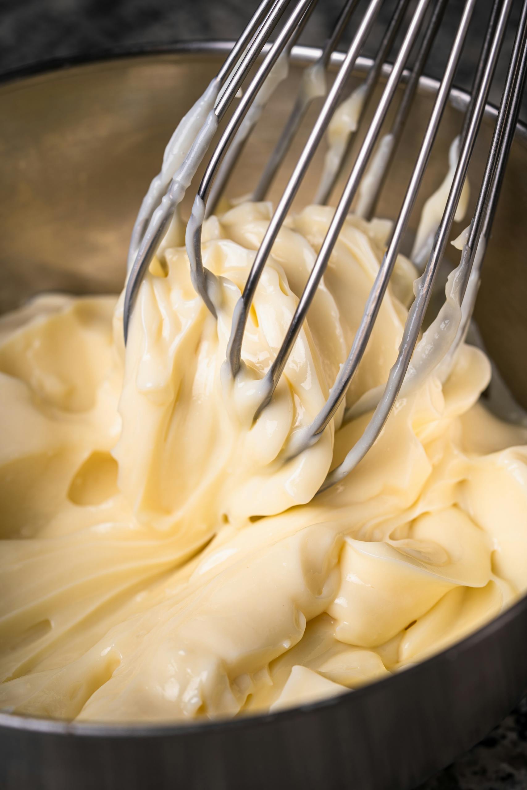 Close-up of homemade mayonnaise being whisked in a metal bowl.