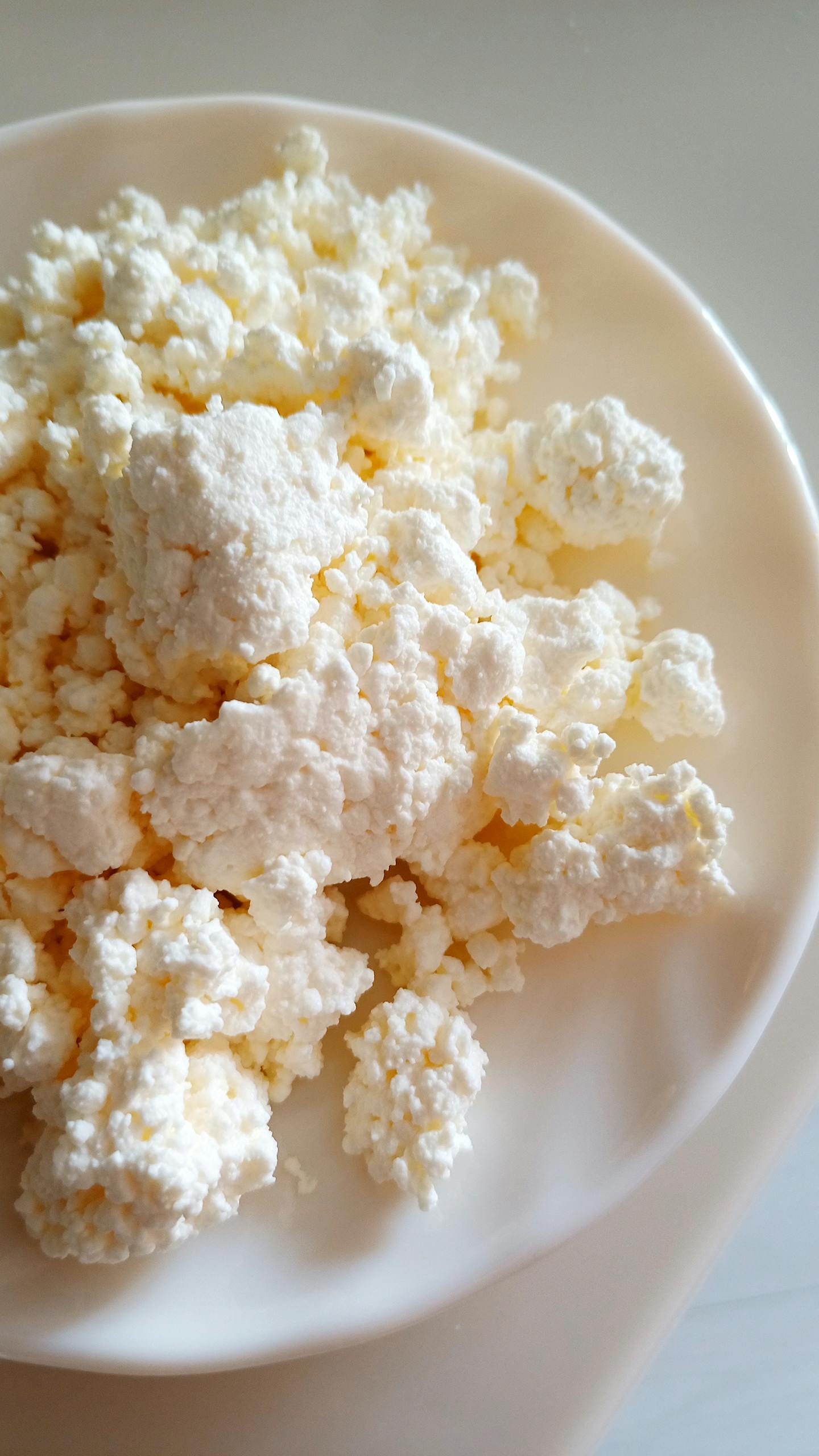 Fresh cottage cheese on a white plate, showing texture and detail.