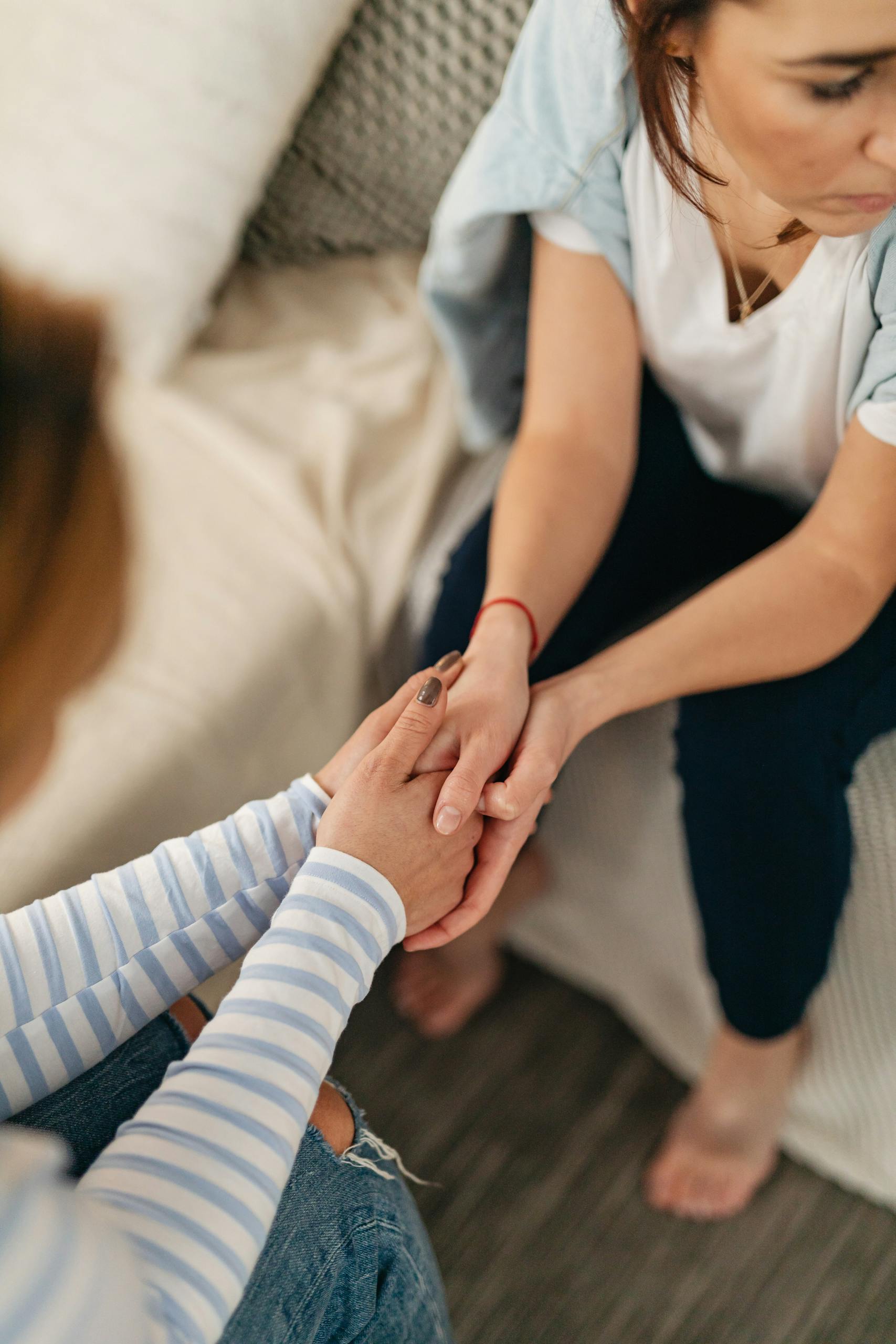 Two women showing support and empathy by holding hands in a cozy indoor setting.